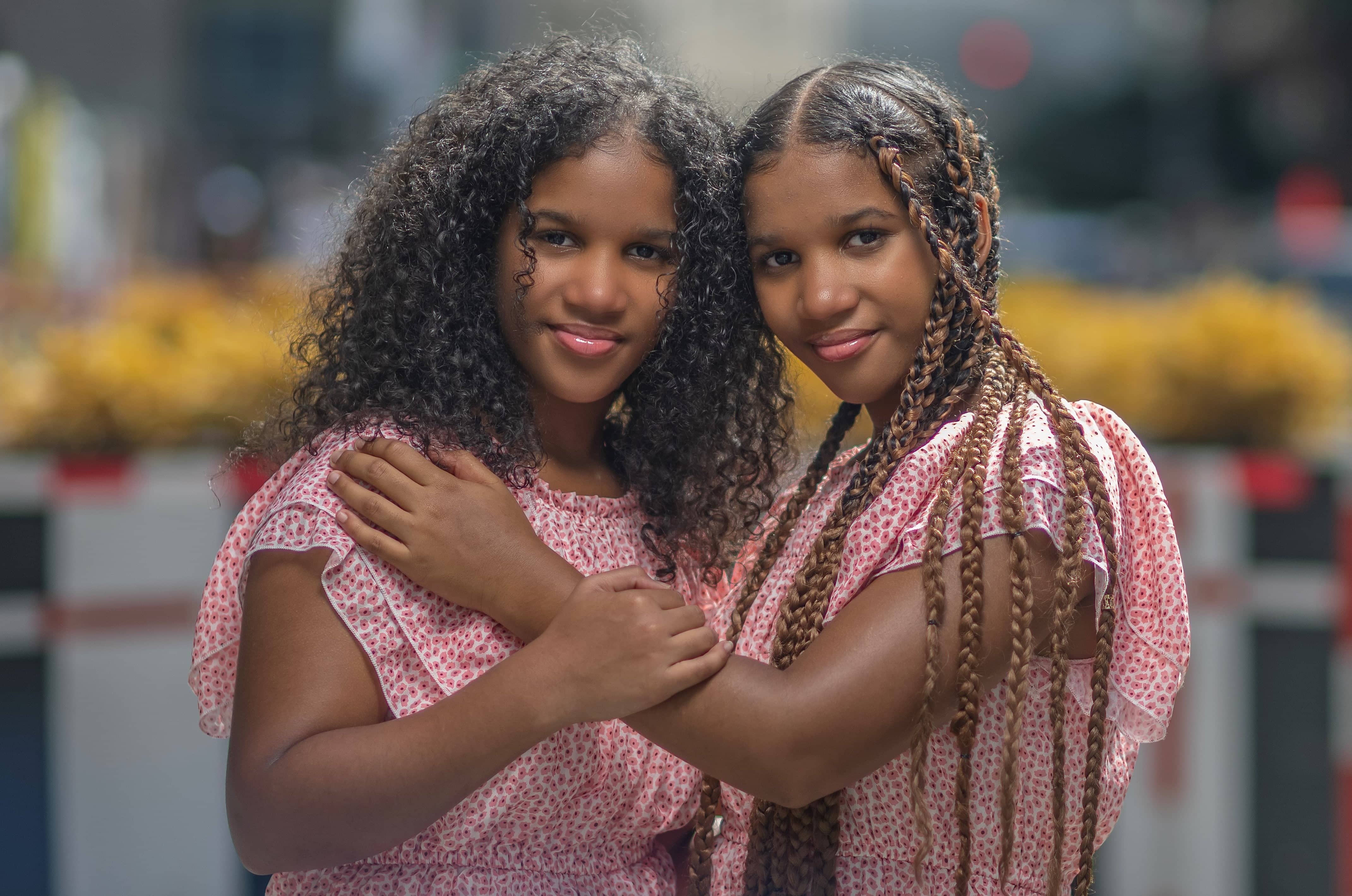 Andrea and Selena Alphonse pose next to each other in pink floral dresses. The picture is taken from the waist up.